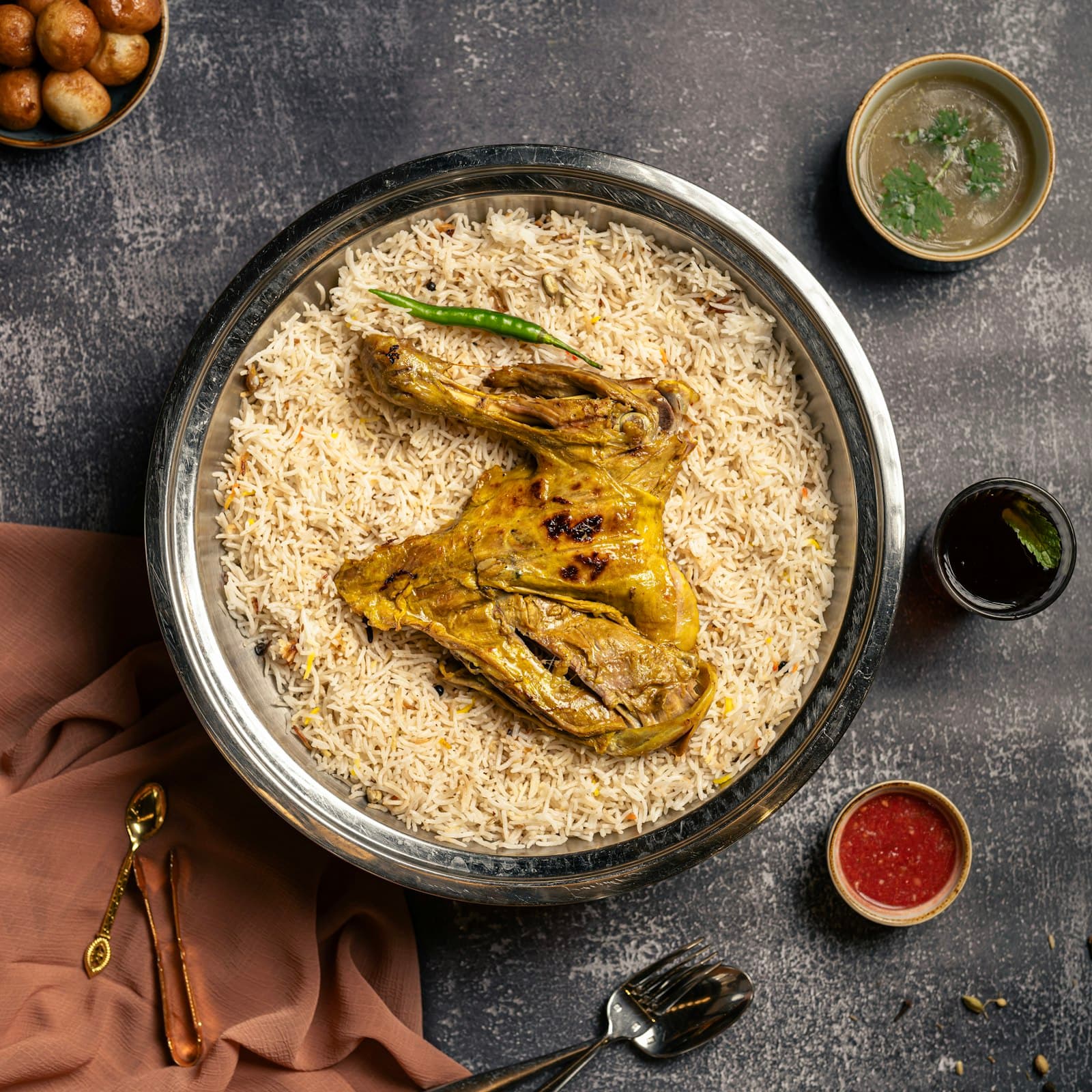 A whole chicken on a tray of Mandi rice, with sauces and salad around it