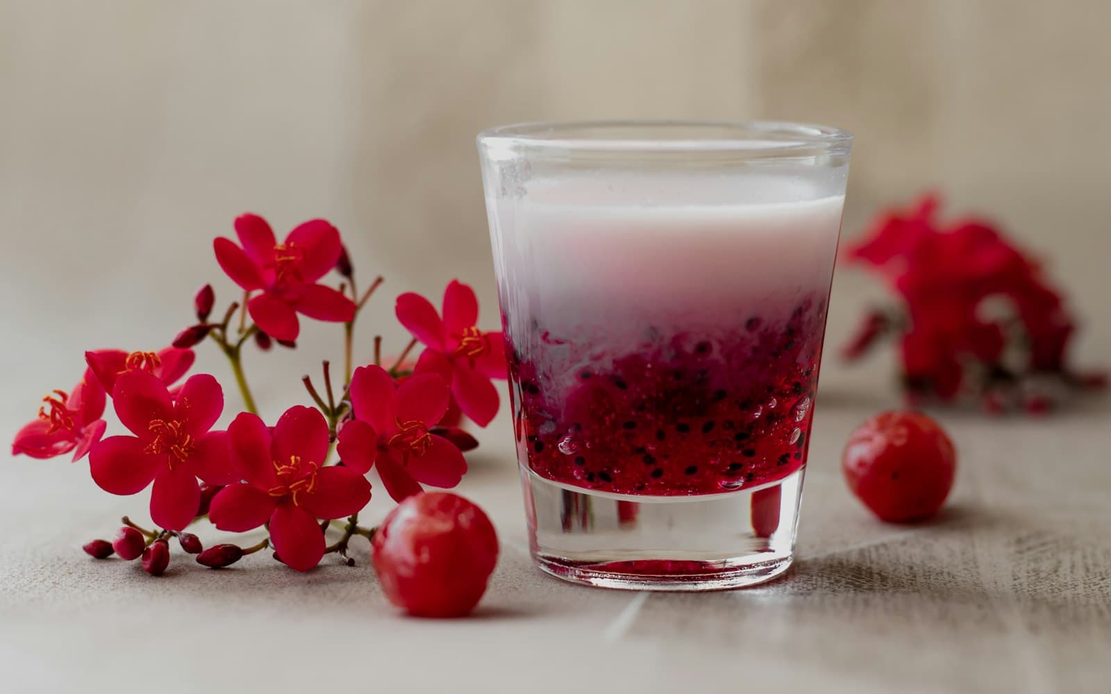 A glass of layered rose falooda surrounded by red flowers