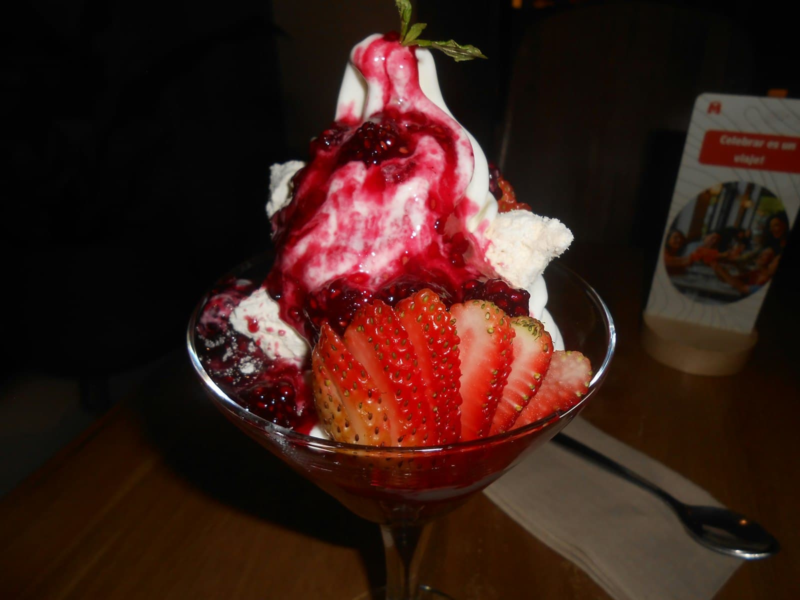 A strawberry dessert glass with cream, berry sauce and fresh strawberries