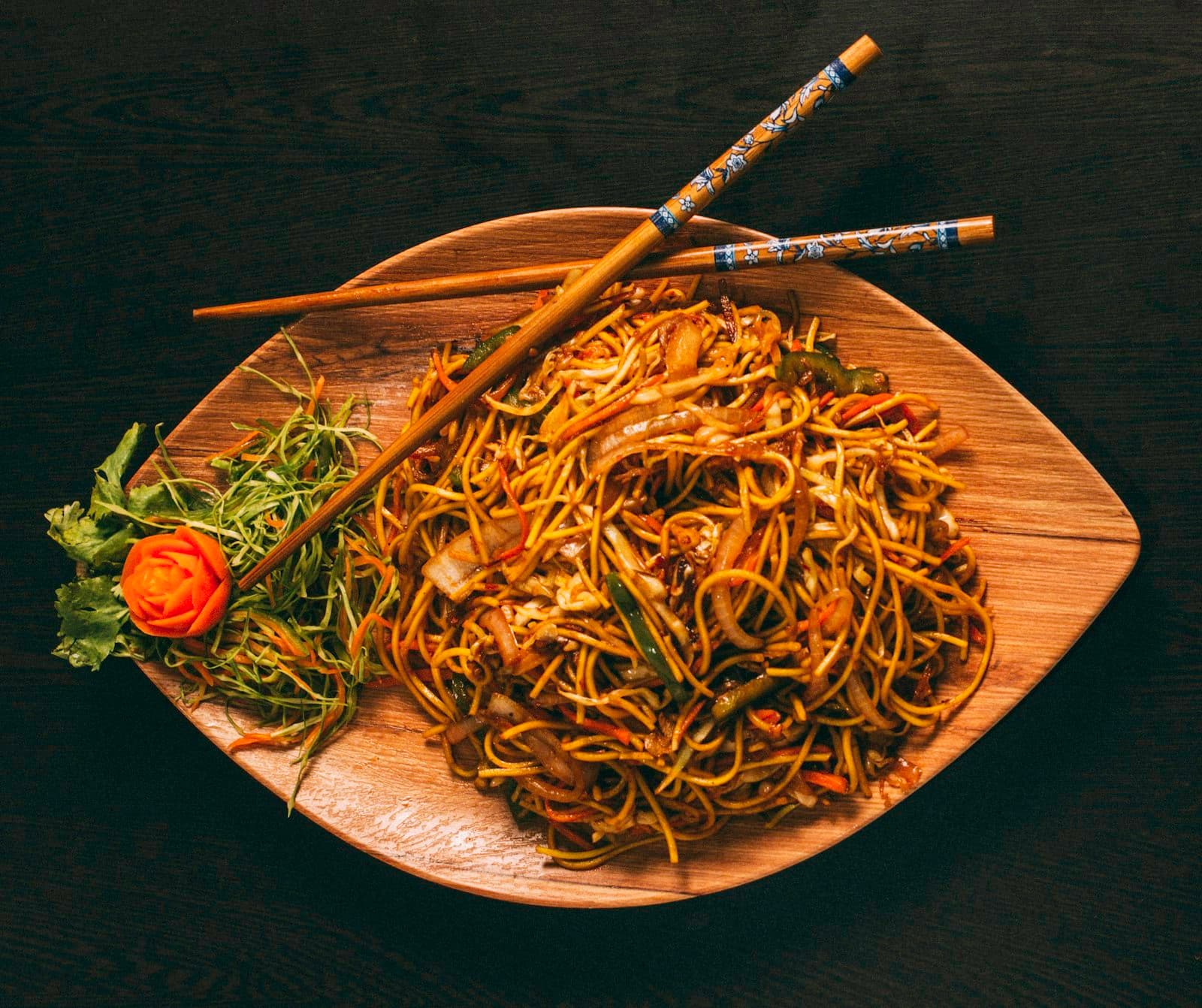 Stir-fried noodles with vegetables on a wooden plate